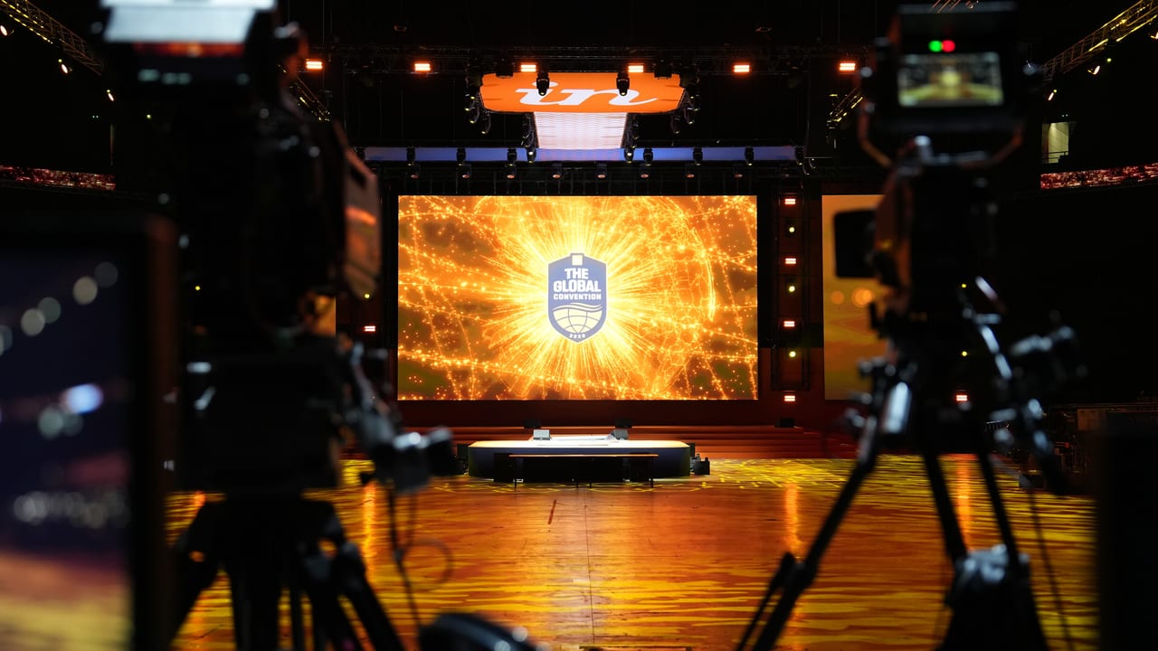 Broadcast cameras on a riser framing a stage and LED wall before doors