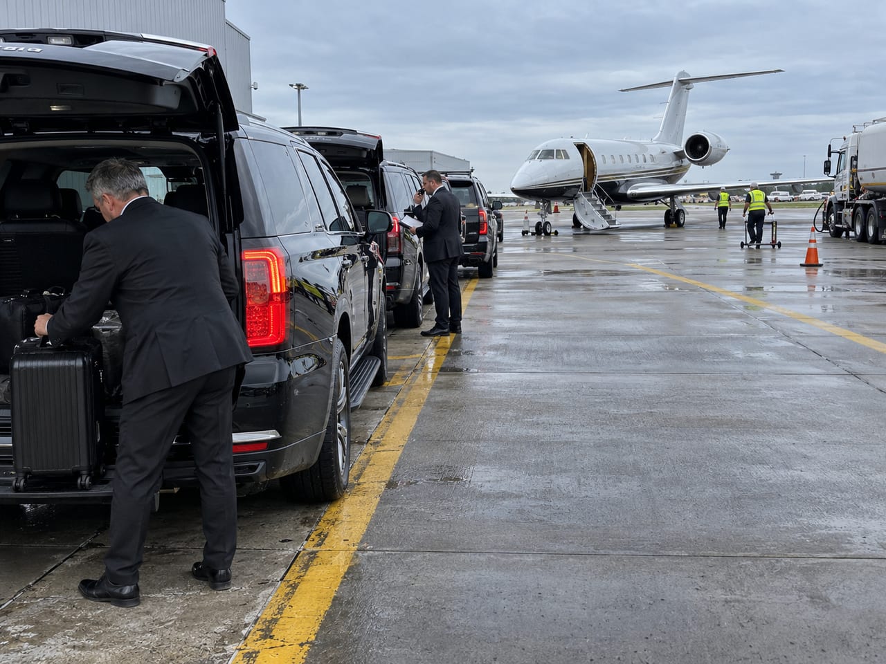 Black SUVs on the apron beside a private jet, a driver loading a suitcase