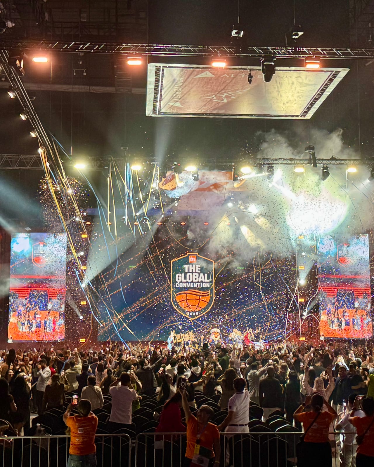 Belgrade Arena during the inCruises Global Convention: confetti and streamers fall in front of a wide LED stage showing the Global Convention emblem, lit by truss-mounted beams over a crowd with raised arms