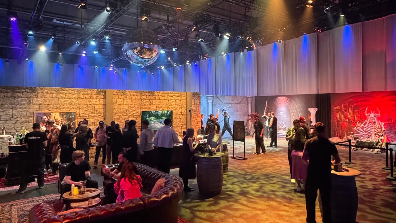 Lounge hall at the Masters of the Universe activation in Berlin: creators gathered around chesterfield sofas and barrel tables beneath a lighting rig and disco ball, with themed set walls along the back