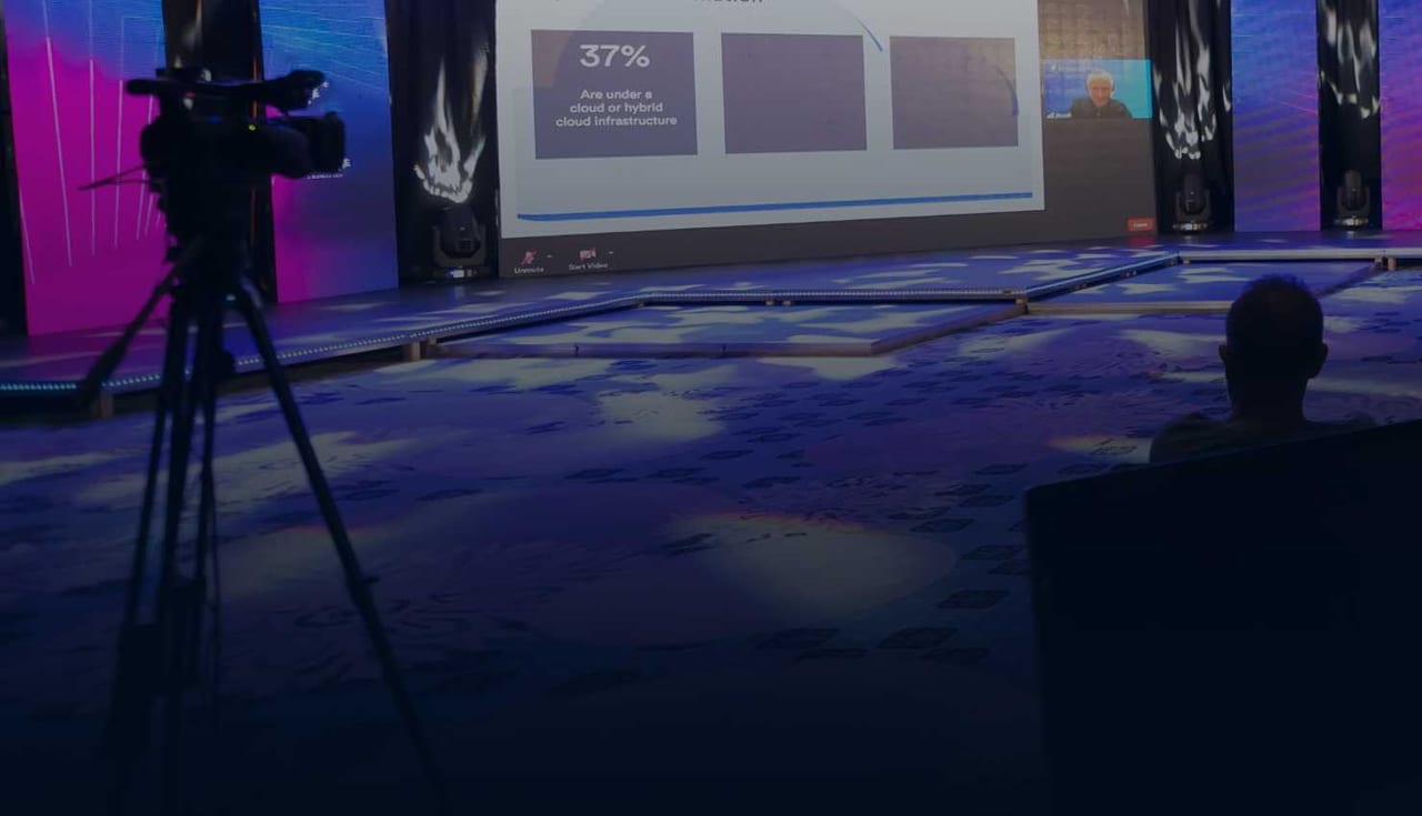 Stage at the Nexora event with LED walls, a presentation screen and camera operators on tripods in a purple-lit hall
